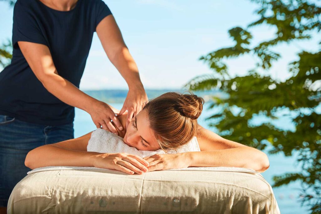Frau genießt eine Outdoor-Massage im Garten am See
