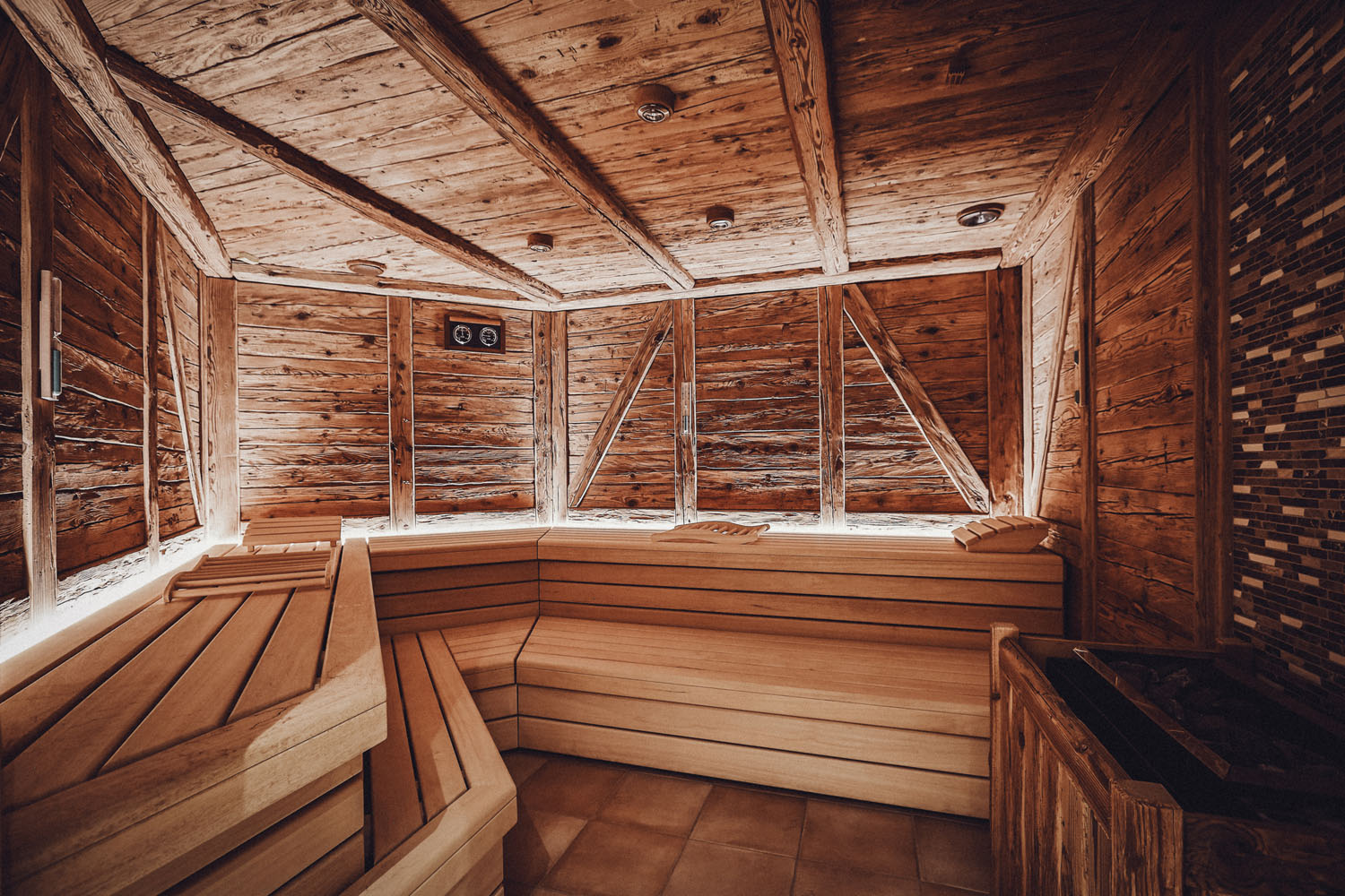 Eine geräumige, rustikale Holzsauna mit abgestuften Sitzbänken, warmer Beleuchtung und holzgetäfelten Wänden und Decken, die eine gemütliche und einladende Atmosphäre schaffen.