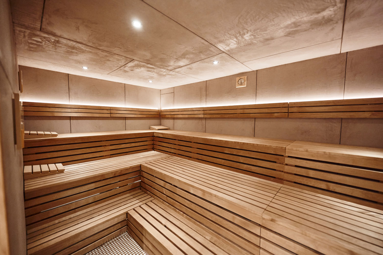 Sauna mit Holzvertäfelung, gestuften Sitzgelegenheiten, sanfter indirekter Beleuchtung und einem modernen, klaren Design.