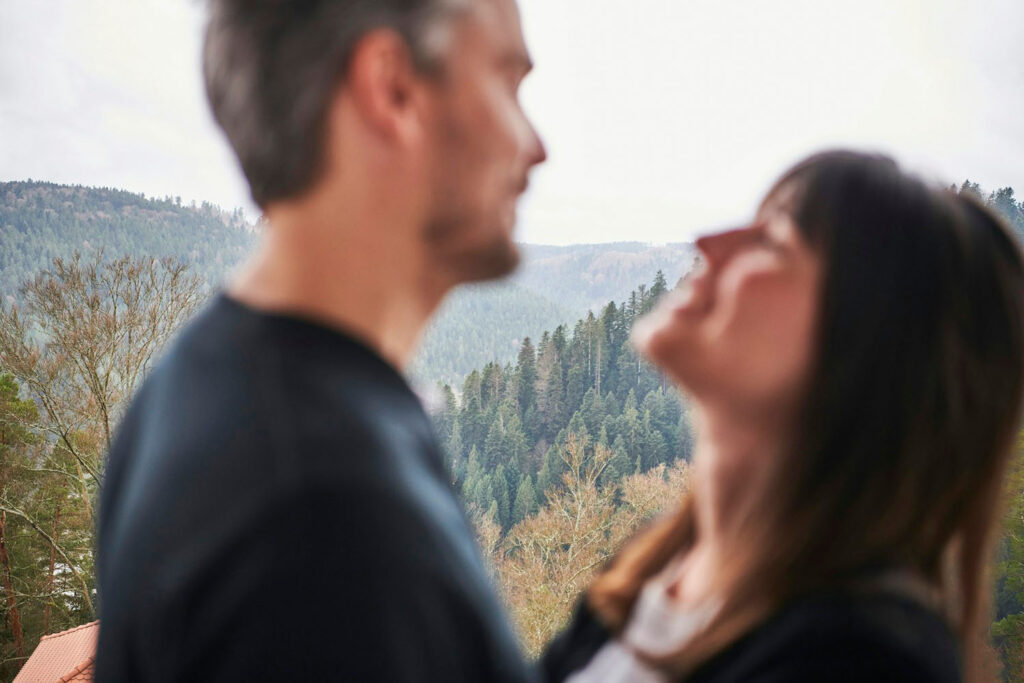 Ein unscharfes Bild von zwei Menschen, die dicht beieinander stehen, vor dem Hintergrund einer bewaldeten Berglandschaft.