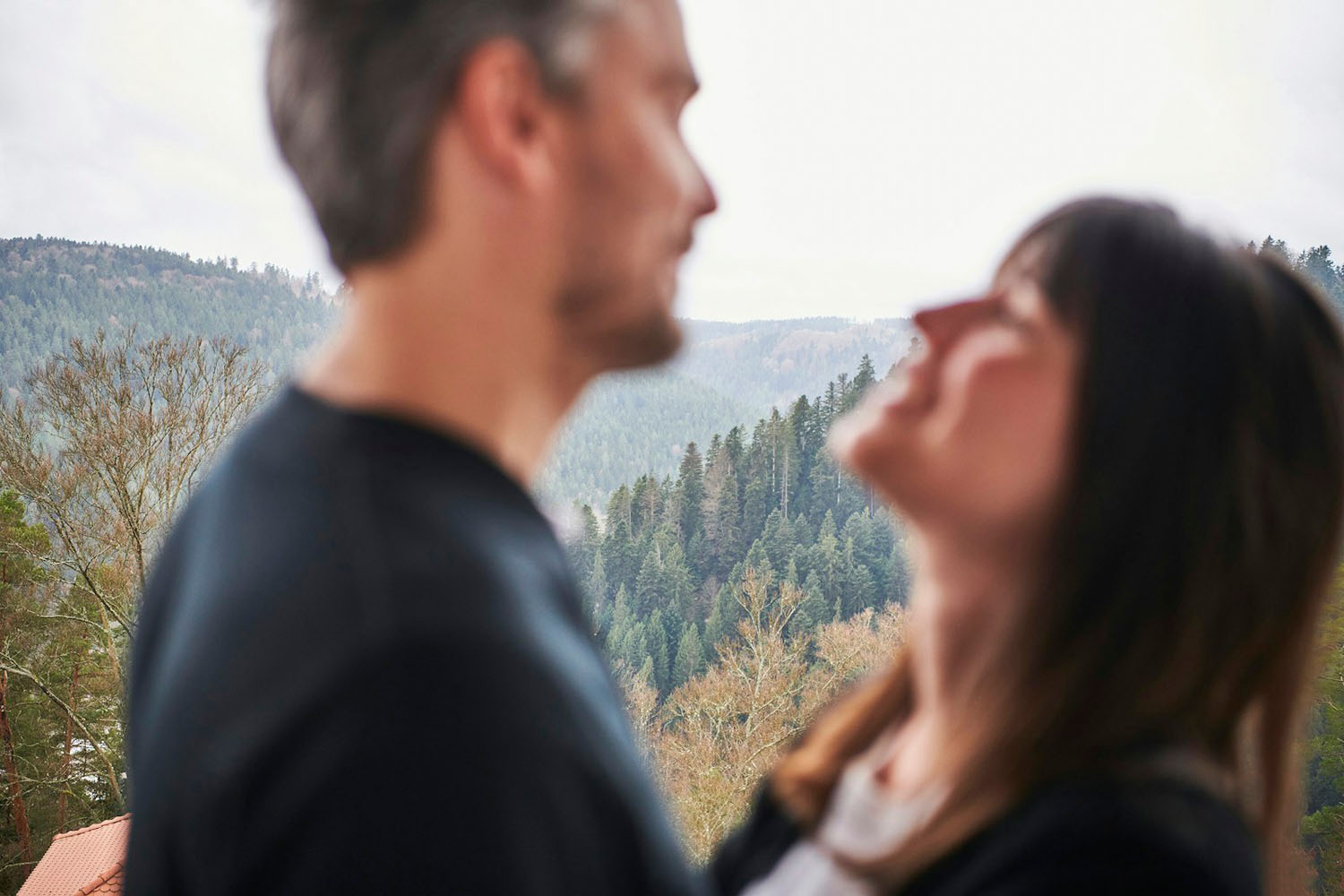 Ein unscharfes Bild von zwei Menschen, die dicht beieinander stehen, vor dem Hintergrund einer bewaldeten Berglandschaft.