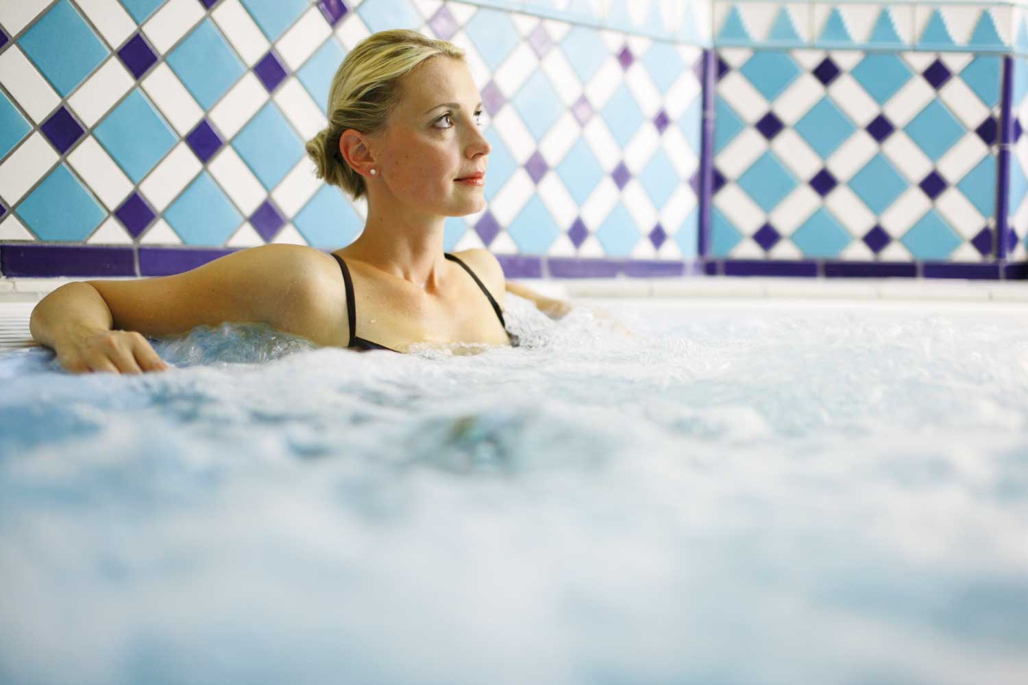 Eine Frau, die sich in einem sprudelnden Whirlpool vor einer blau-weiß gekachelten Wand entspannt.